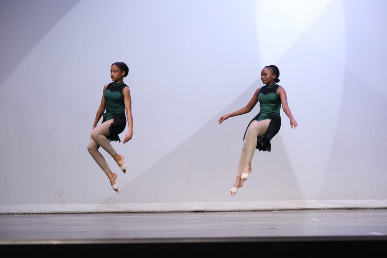 Two dancers in green leaping on stage