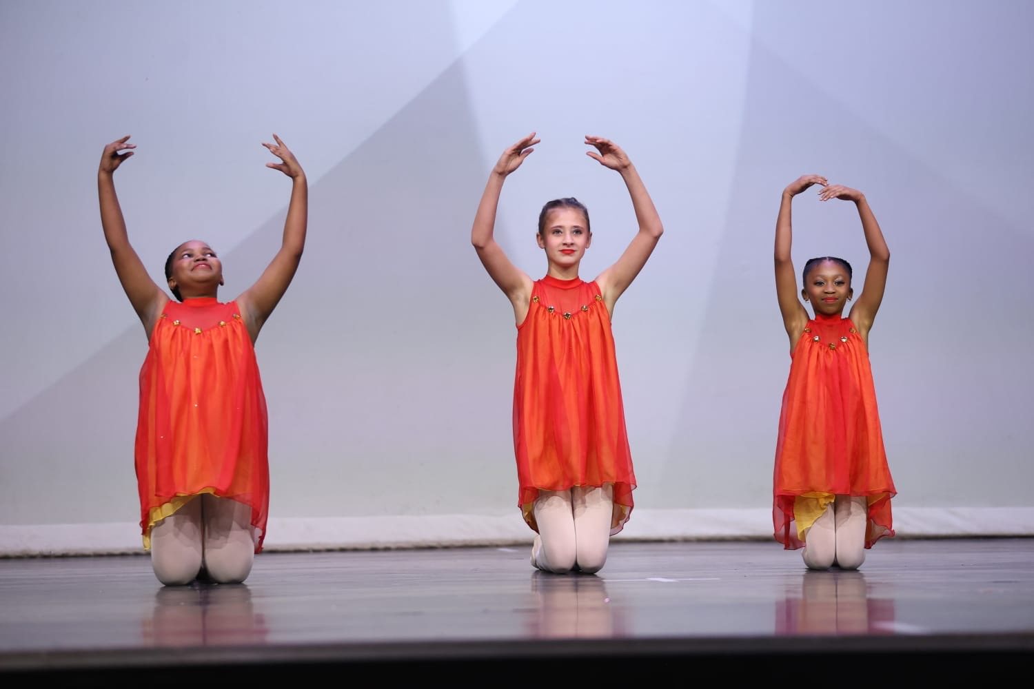 Three dancers in orange performing together on stage