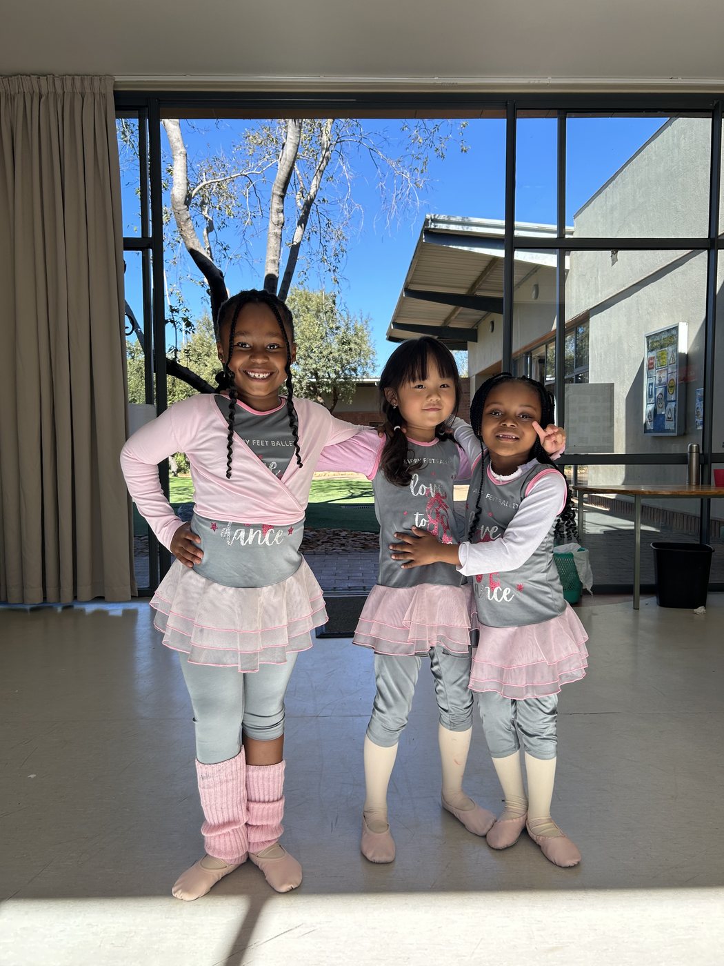 Three young dancers in pink smiling at the studio